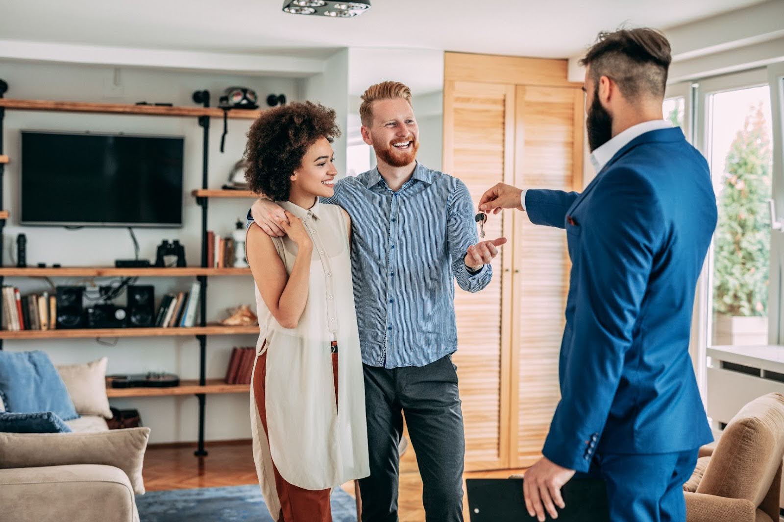 A person who helps with loan programs for first-time home buyers handing a couple the keys to their new property